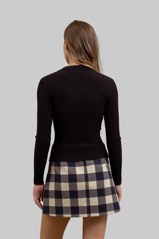 Person wearing a black sweater and plaid skirt against a green background