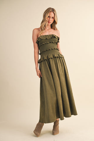 Woman wearing an olive green strapless dress with ruffled details on a beige background