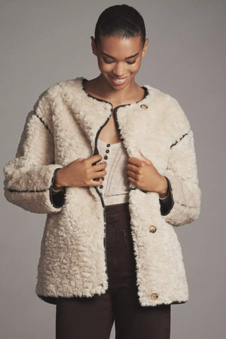 Woman wearing a cream-colored sherpa jacket against a gray background