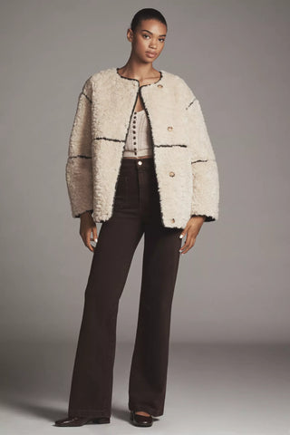 Woman wearing a textured beige jacket and dark pants against a gray background