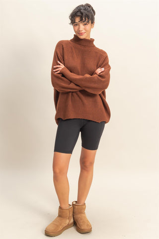 Person wearing a brown sweater, black shorts, and tan boots on a beige background
