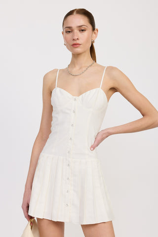 Front view of a woman wearing a white mini dress with thin straps, a button-down bodice, and a pleated skirt