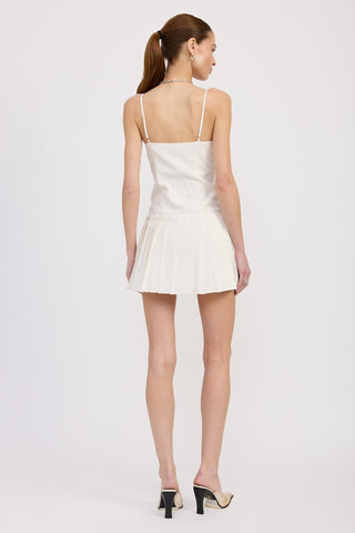 Back view of a woman wearing a white mini dress with spaghetti straps and a pleated skirt