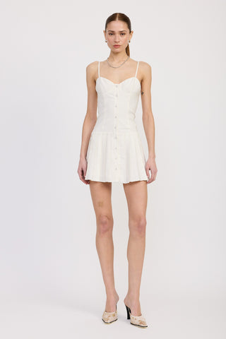 Full-length front view of a woman wearing a white strappy mini dress with button-down front and pleated skirt