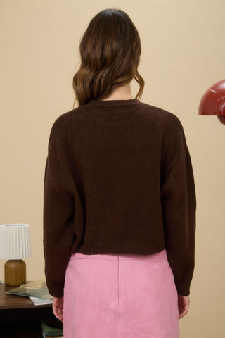 Person wearing a brown sweater and pink pants against a beige wall.