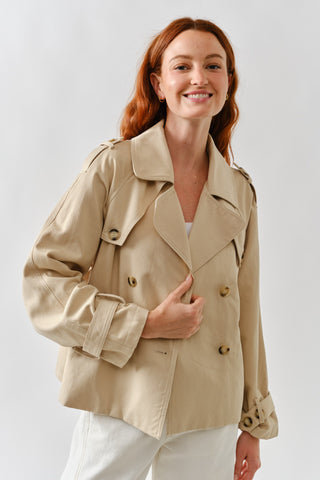 Woman wearing a beige trench coat against a plain background