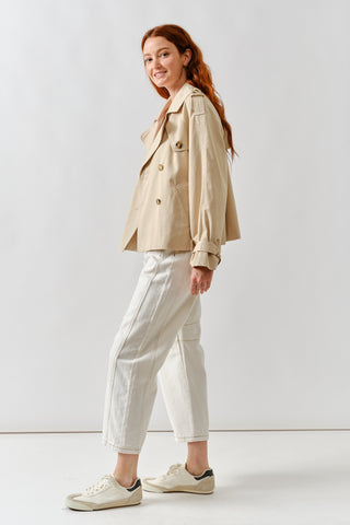 Woman wearing a beige jacket and white pants on a plain background