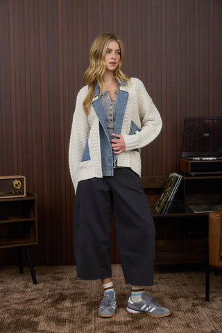 Woman wearing a white cardigan over a denim shirt in a room with wooden paneling.