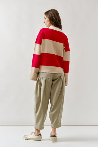 Person wearing a red and beige striped sweater with beige pants on a white background