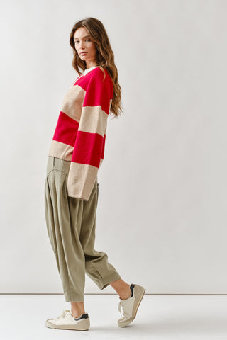 Woman wearing a red and beige striped sweater with beige pants against a white background
