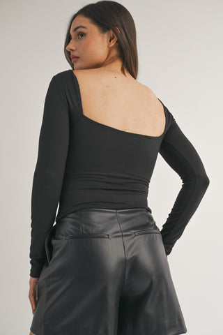 Woman wearing a black one-shoulder top and leather shorts on a plain background