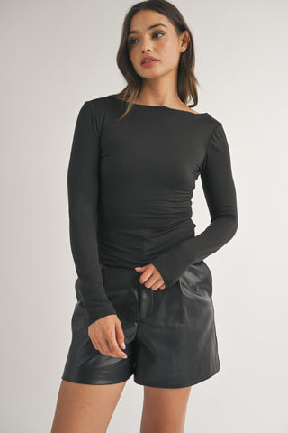 Woman wearing a black long-sleeve top and black leather shorts on a light gray background