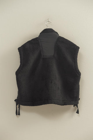 Black fleece vest on a hanger against a beige wall