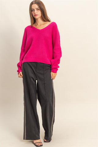 Woman wearing a bright pink sweater and black pants on a beige background
