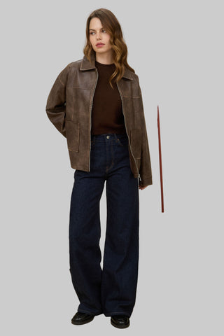 Woman wearing a brown leather jacket and dark jeans on a plain background