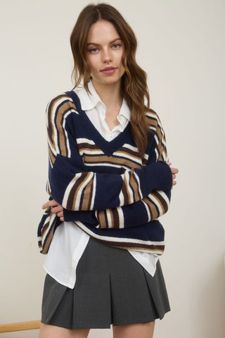 Woman wearing a striped sweater over a white shirt and black skirt against a plain background