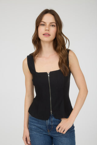 Woman wearing a black sleeveless top with a zipper and blue jeans on a white background