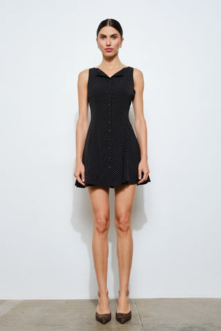 Woman wearing a black sleeveless dress with white polka dots against a white background