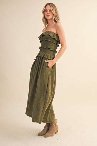 Woman wearing an olive green strapless top and long skirt with beige boots on a beige background