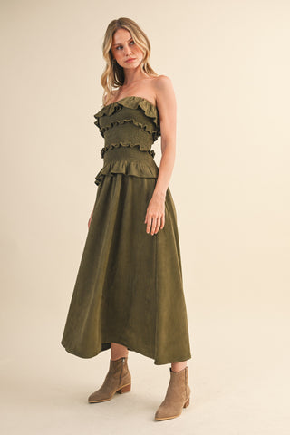 Woman wearing an olive green strapless dress with ruffled top on a beige background
