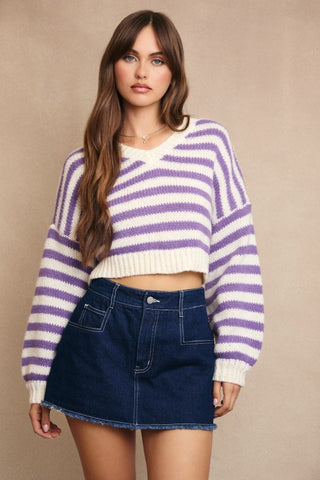 Woman wearing a purple and white striped sweater with a denim skirt on a beige background
