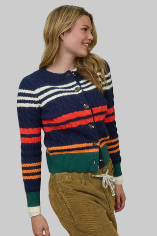 Woman wearing a colorful striped sweater and green pants against a green wall.