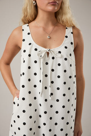 Woman wearing a white sleeveless top with black polka dots against a neutral background