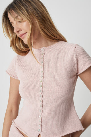 Woman wearing a pink textured top with buttons on a plain background