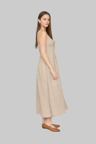 Woman in a beige checkered dress standing in a room with blue shutters and decorative elements.