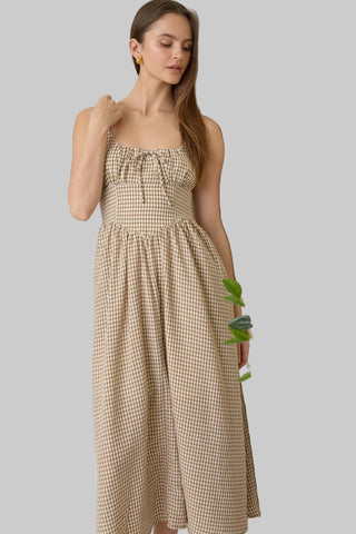 Woman in a checkered dress standing next to a lemon tree indoors.
