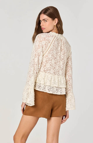 Woman wearing a white lace top and brown shorts on a light gray background