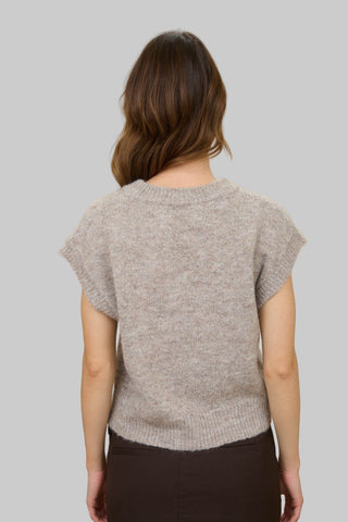 Woman wearing a light gray knitted top against a beige background