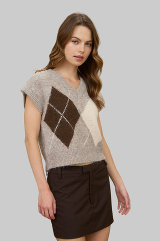 Woman wearing a argyle patterned sweater and skirt in a room with a lamp and books.