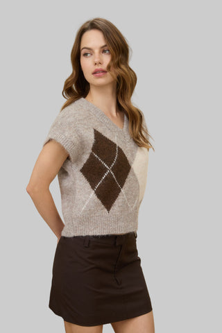 Woman wearing an argyle  patterned sweater in a room with a lamp and desk.