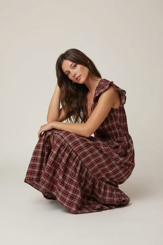 Woman in a plaid dress sitting on a path in a garden.