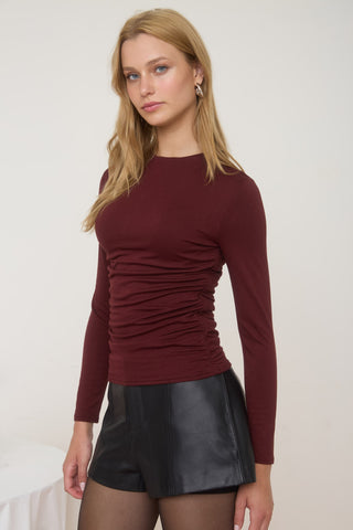 Woman wearing a burgundy long-sleeve top and black leather skirt against a white background