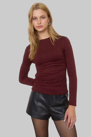 Woman wearing a burgundy long-sleeve top and black leather shorts on a gray background