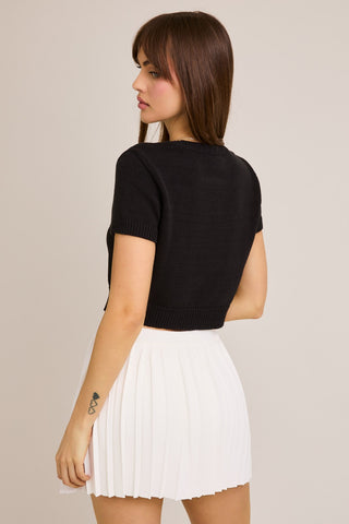 Woman wearing a black top and white pleated skirt on a beige background