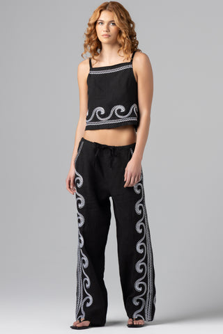 Woman wearing a black top and pants with white patterns on a gray background