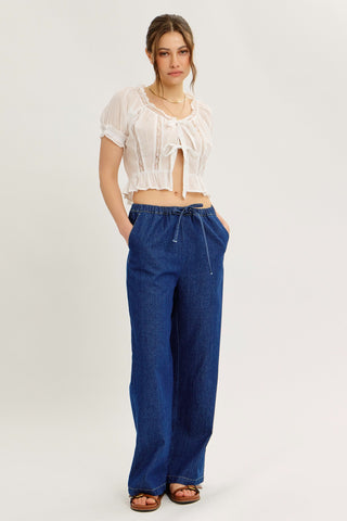Model wearing blue denim drawstring pants with full outfit, showing off front pockets.