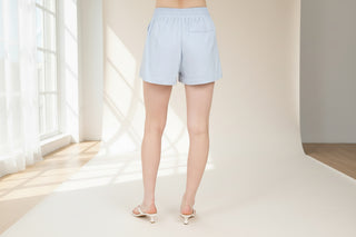 Light blue shorts worn by a person on a beige background with wicker furniture.