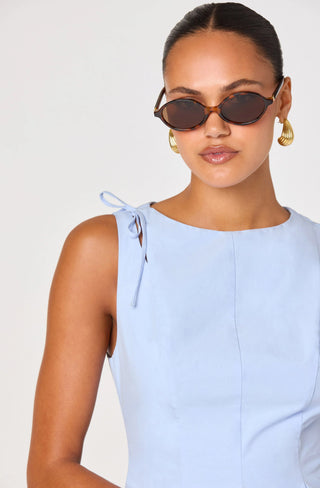 Woman wearing a light blue sleeveless dress with bow details on a plain background