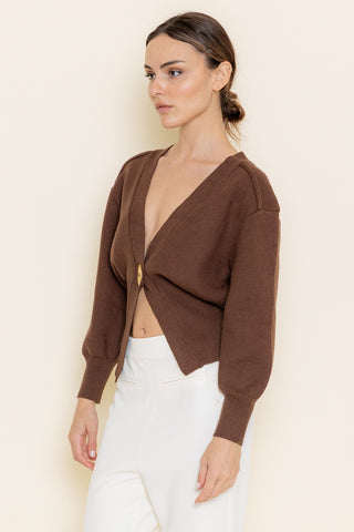 Woman wearing a brown cropped cardigan over a white top against a beige background