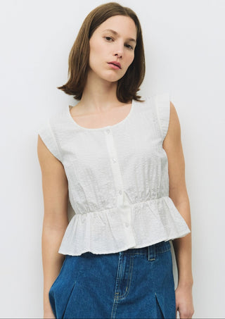 Front view of a white sleeveless cotton top with subtle texture, a button front, and peplum hem, paired with blue denim