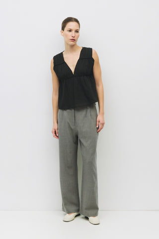 Sleeveless black cotton top with deep V-neck and gathered waist, styled with gray wide-leg trousers and white flats