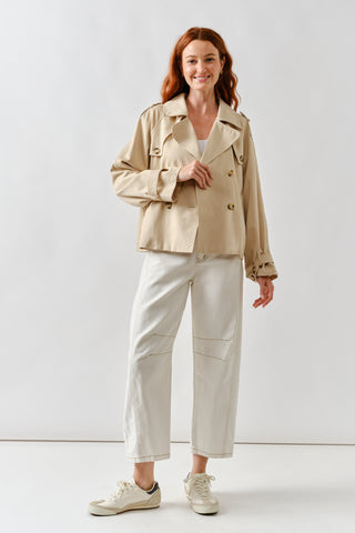 Woman wearing a beige jacket and light-colored pants on a white background
