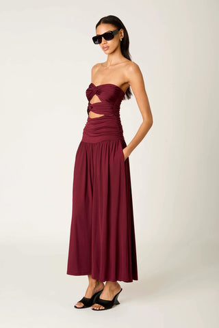 Woman wearing a burgundy strapless dress with cut-out details on a white background