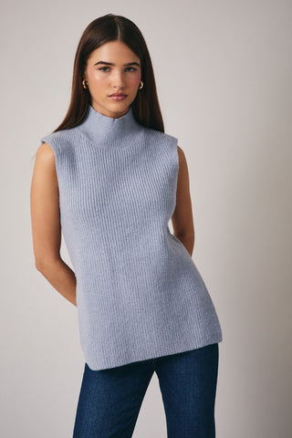 Woman wearing a light blue sleeveless knitted top against a plain background