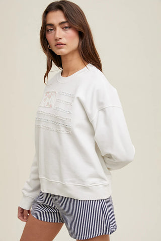 Side view of model wearing a white floral flag pullover sweatshirt with navy striped shorts.