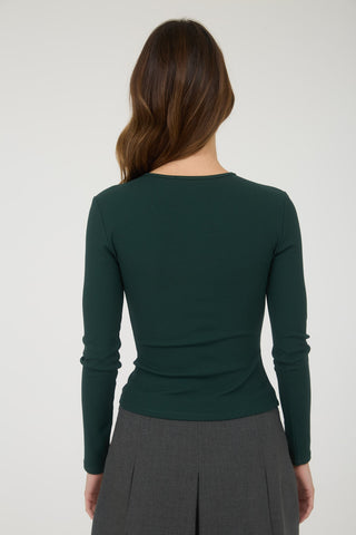 Person wearing a green long-sleeve top and gray skirt on a white background